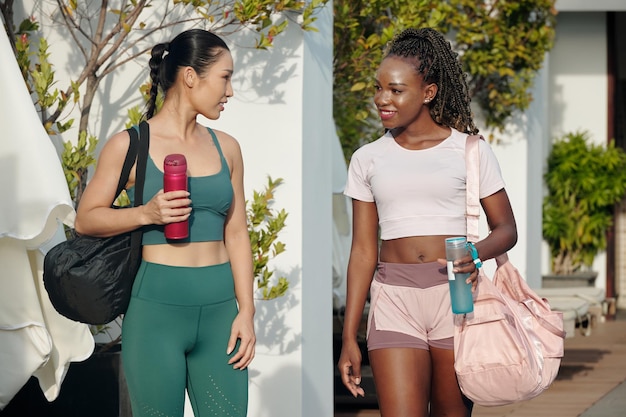 Pretty young female friends drinking water and chatting when walking home after working out together...