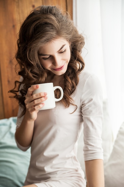 飲み物と一緒にカップを持っているかなり若い女性。垂直屋内ショット。