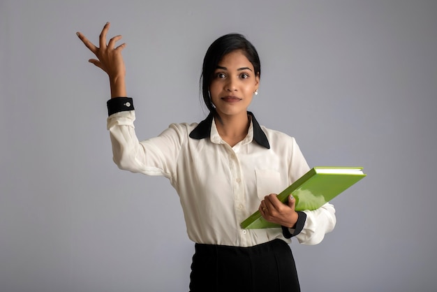 Pretty young girl holding book and posing on grey wall