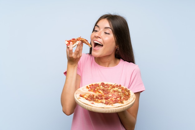 Foto ragazza graziosa che tiene una pizza sopra la parete blu isolata