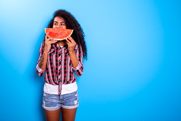 Ragazza graziosa che tiene fetta di anguria davanti al suo viso. ritratto della ragazza afroamericana sorridente isolata sana e felice