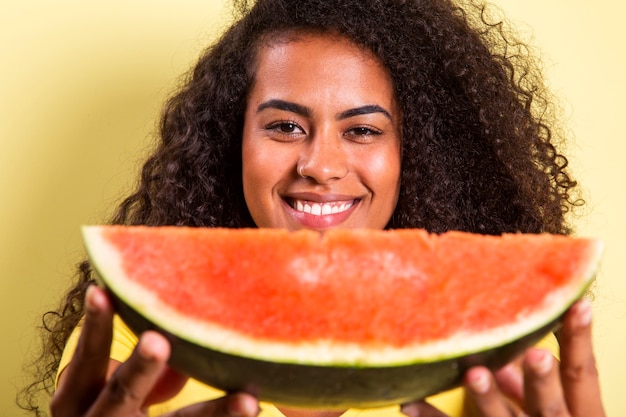 Ragazza graziosa che tiene fetta di anguria davanti al suo viso. ritratto della ragazza sorridente dell'afroamericano isolata