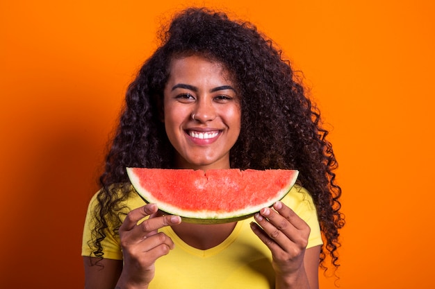 Pretty young girl holding slice of watermelon in front of her face. Portrait of smiling african american girl isolated