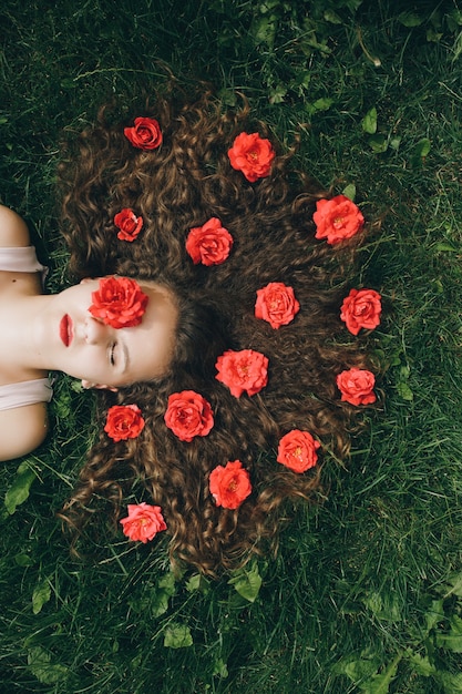 Foto ragazza graziosa che posa all'erba con i fiori nei suoi lunghi capelli ricci sparsi