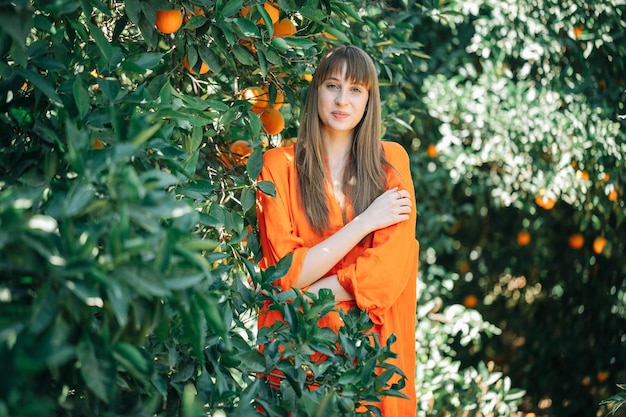 Pretty young girl in orange dress is looking at camera in orange garden