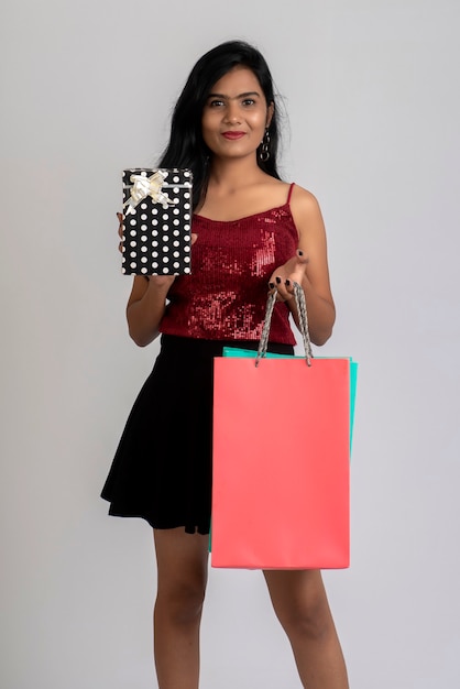 Pretty young girl posing with shopping bag and gift box on a grey background