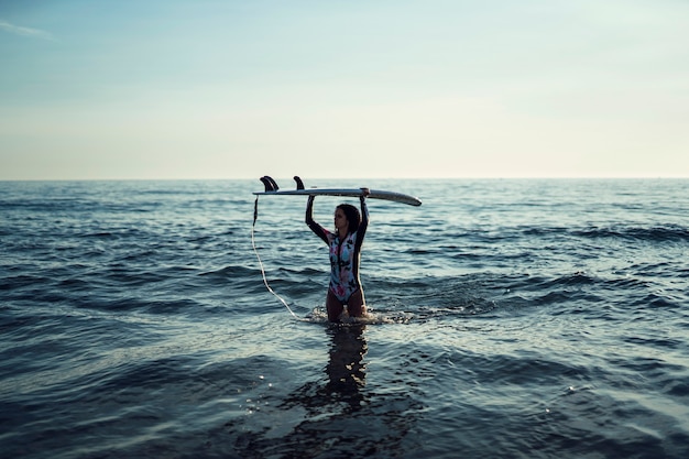 pretty young girl in the sea holding a surfboard above her head