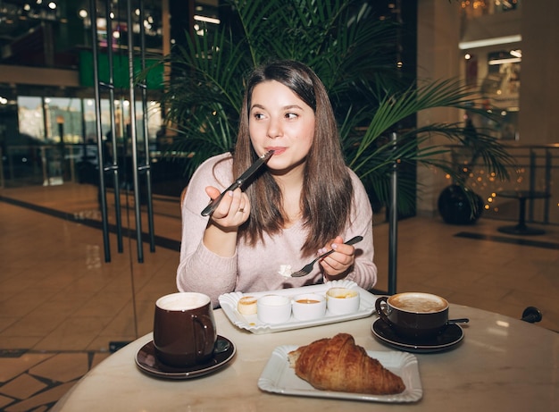 カフェでコーヒーを飲みながら座っているかわいい若い女の子素敵な女性はコーヒーで朝食を楽しんでいます