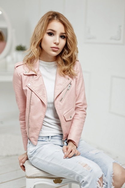 Pretty young girl in stylish pink leather jacket in white room