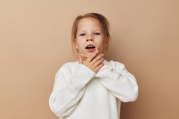 Pretty young girl in white sweater posing hand gestures beige background