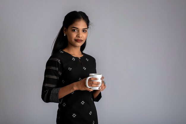 Pretty young girl with a cup of tea or coffee posing on grey background