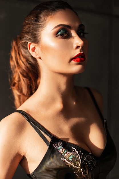 Bella ragazza con labbra rosse e trucco in abiti di moda al chiuso al tramonto