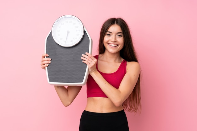 Pretty young girl with weighing machine over isolated pink wall with weighing machine