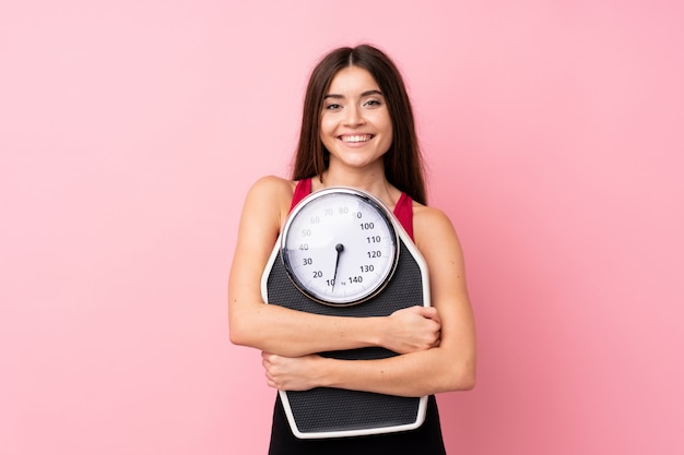 Pretty young girl with weighing machine over isolated pink wall with weighing machine