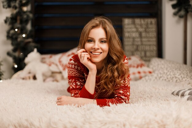 Pretty young happy woman in a red fashion sweater lies on the bed and enjoys the moment