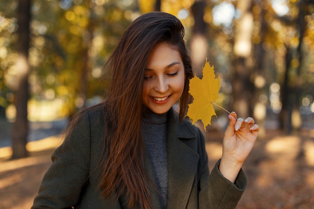 Pretty young happy woman with a smile with a yellow autumn leaf walks in the park on a sunny day