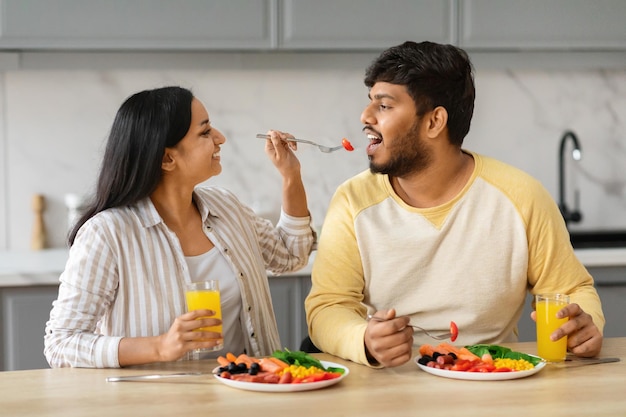 美しい若いインド人女性が夫にキッチンのインテリアを食べさせています