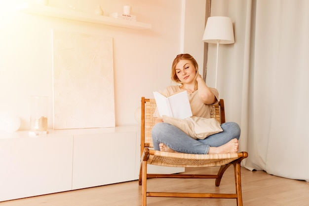 Pretty young lady sitting in the armchair reading book