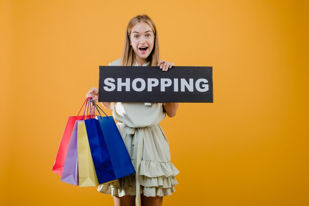 Pretty young lady with shopping sign and colorful shopping bags isolated over yellow