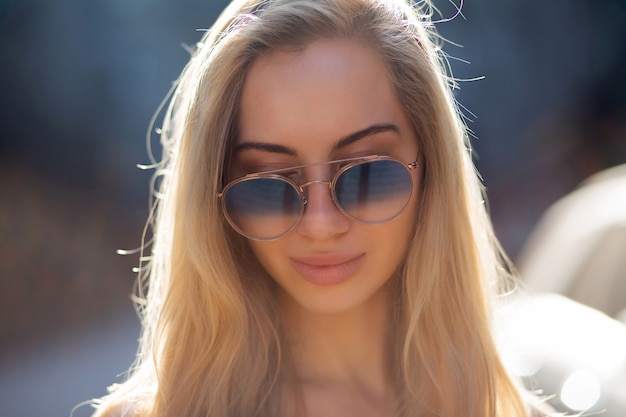 Pretty young model with long hair wearing glasses, posing at the street in sunny day