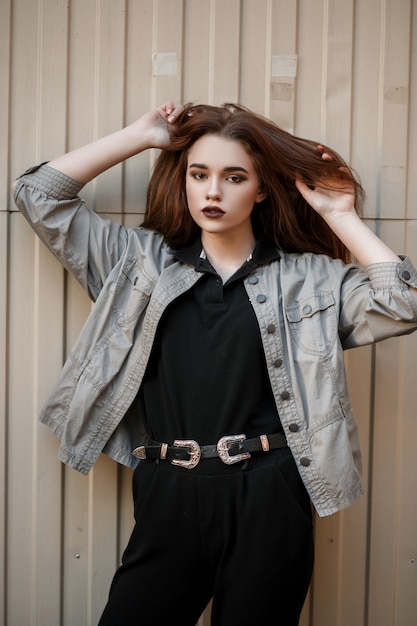 유행 재킷과 검은 색 폴로에 꽤 젊은 모델 여자는 거리에 금속 벽 근처에 포즈