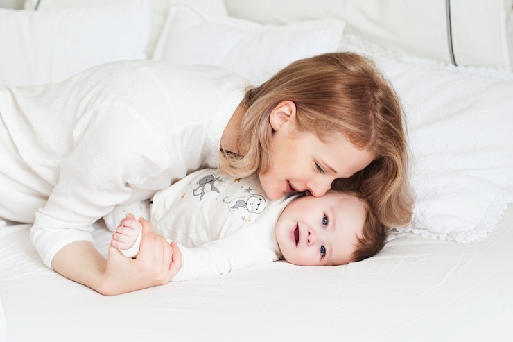 Photo ベッドに幼い息子を持つかなり若い母親。面白い笑顔の朝。白い寝室