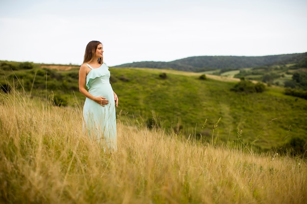 Pretty young pregnant woman relaxing outside in nature at summer day