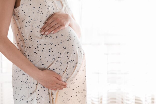 Foto una bella giovane donna incinta in piedi vicino alla finestra di casa