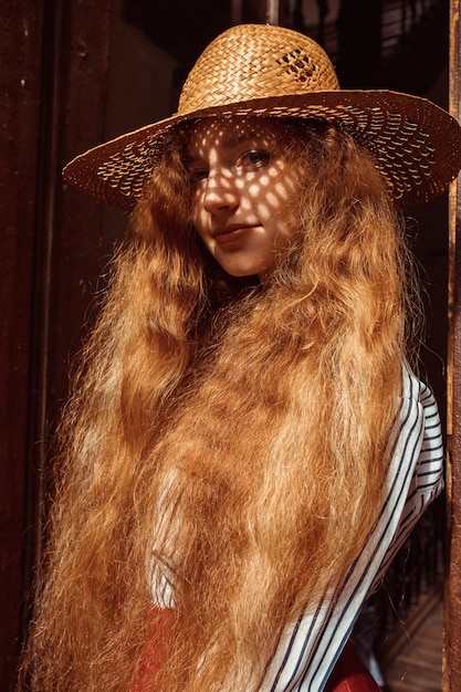 彼女の顔に影のある麦わら帽子のかなり若い赤い髪のモデル