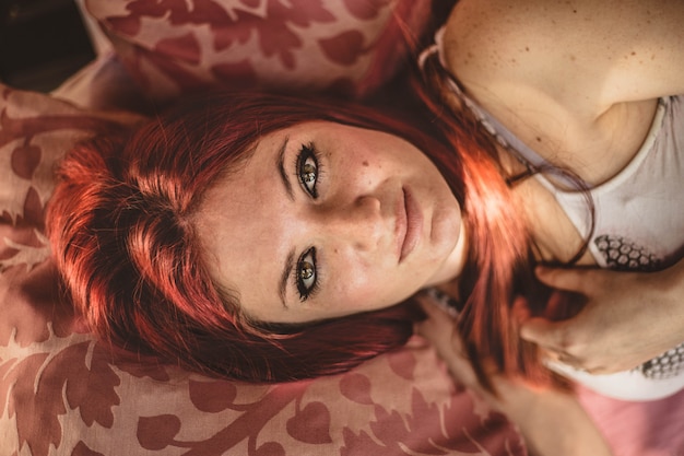 Pretty young redhead woman with beautiful green eyes lying on the sofa serious