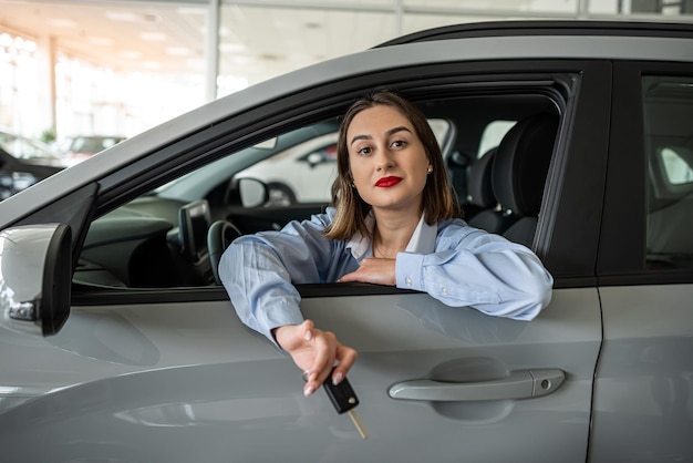 Pretty young saleswoman in elegant suit dealer standing near car at new modern dealership