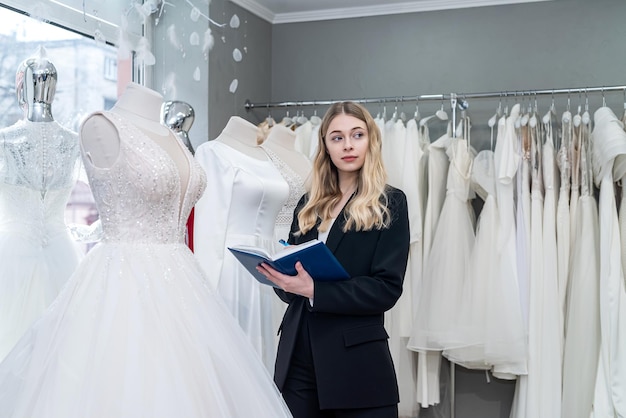 Pretty young saleswoman hold notes diary in modern wedding store Female bridal store