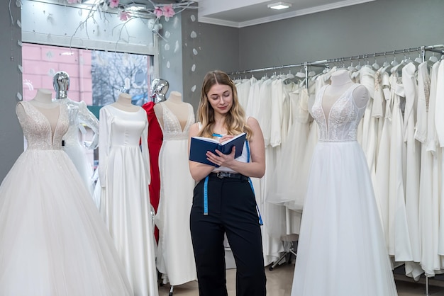 Pretty young saleswoman hold notes diary in modern wedding store Female bridal store