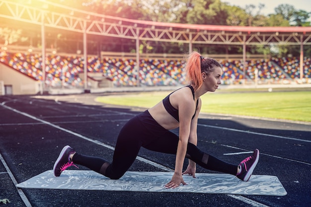 Pretty young slim woman in sportswear doing stretching in stadium before work day