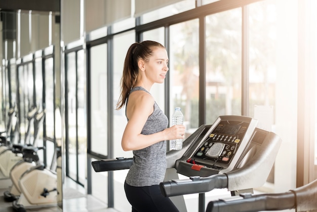 Photo pretty young sport woman is drinking water on treadmill in gym, healthy lifestyle