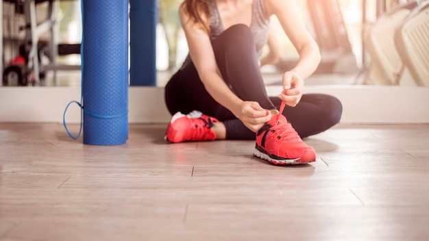 Pretty young sport woman is tying her sneakers in gym, Healthy lifestyle 