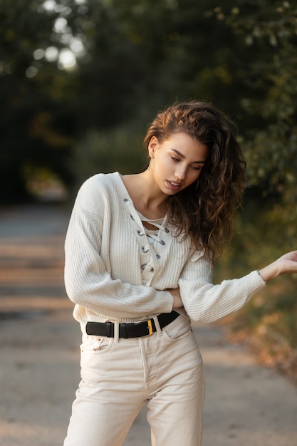 Donna alla moda abbastanza giovane con capelli ricci in un maglione lavorato a maglia in natura. volto femminile carino