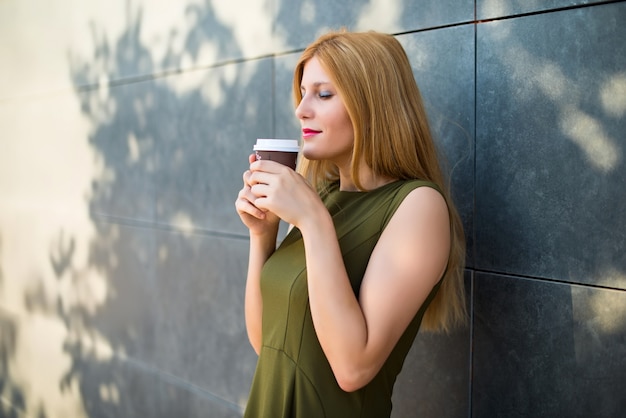 Pretty young teenager girl holding hot coffee in takeaway paper cup at strret