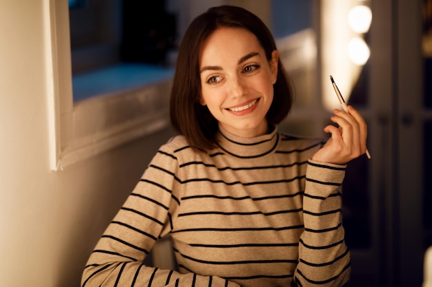 Pretty young woman applying makeup at home