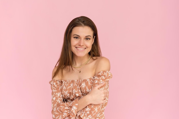 Pretty young woman in a beige dress on a pink background with copy space Summer concept