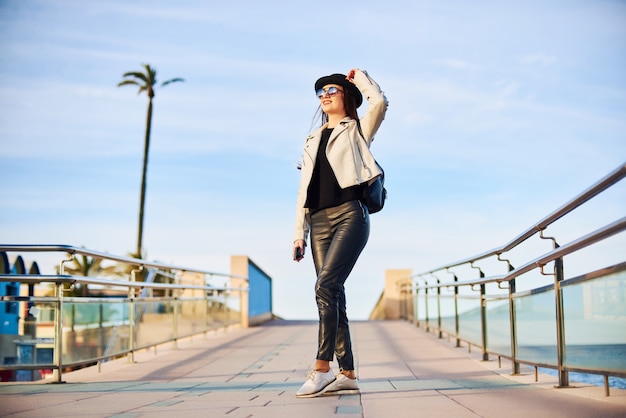 Pretty young woman in black hat walking by the sea