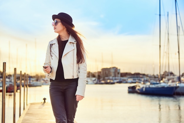 Pretty young woman in black hat with vape at a sea port