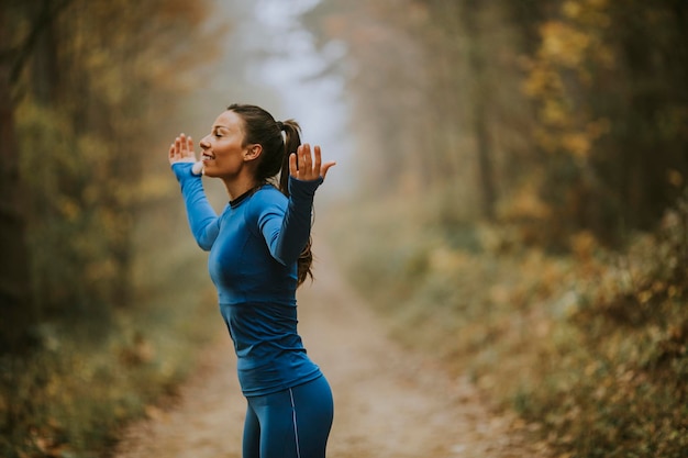 Pretty young woman in blue track suit spreading arms and taking deep breath in a forest