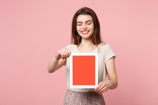 Pretty young woman in casual light clothes posing isolated on pastel pink background studio portrait. People lifestyle concept. Mock up copy space. Holding tablet pc computer with blank empty screen.