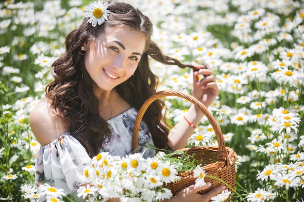 カモミールフィールドのかなり若い女性。花を持つ美しい少女