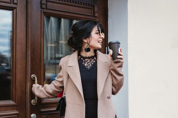 Foto giovane donna graziosa sulla via della città con il telefono cellulare e il caffè