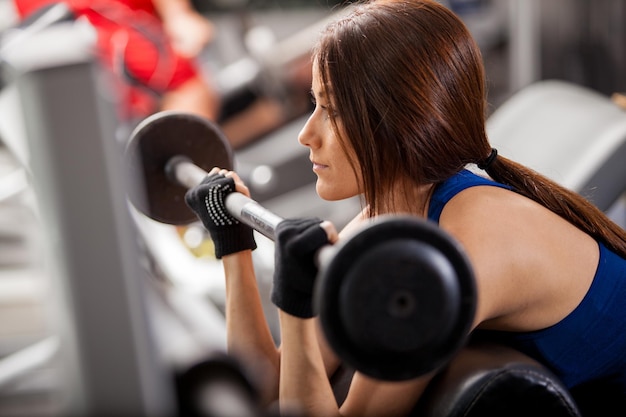 Pretty young woman concentrated in her workout and doing bicep curls in a bench at the gym