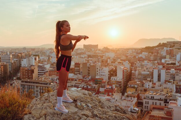 La donna abbastanza giovane fa yoga con vista sulla città al tramonto all'aperto