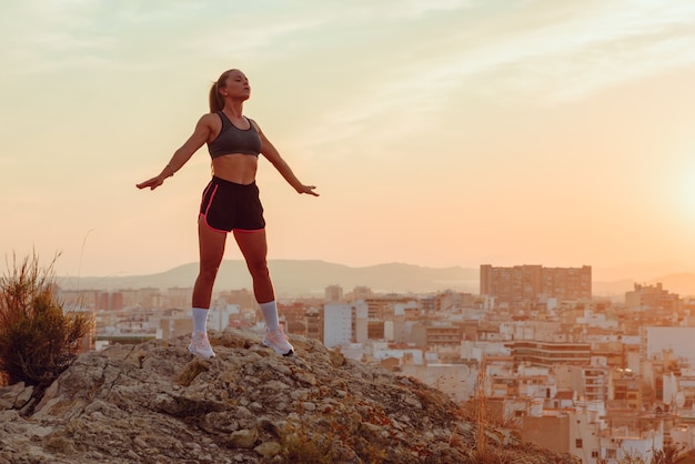 Pretty young woman does yoga overlooking the city at sunset outdoors