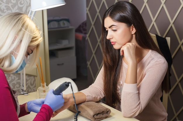 Pretty young woman doing manicure in salon. Beauty concept.